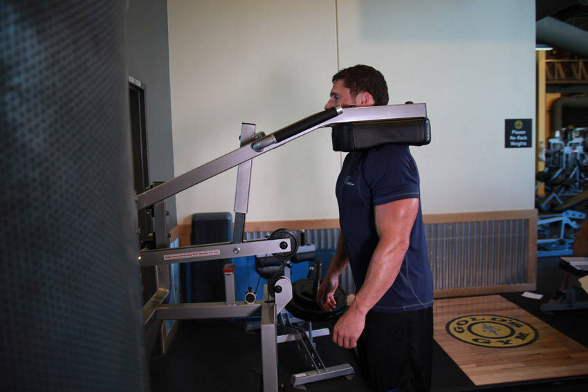 Demonstration of Calf-Machine Shoulder Shrug exercise showing proper form and technique