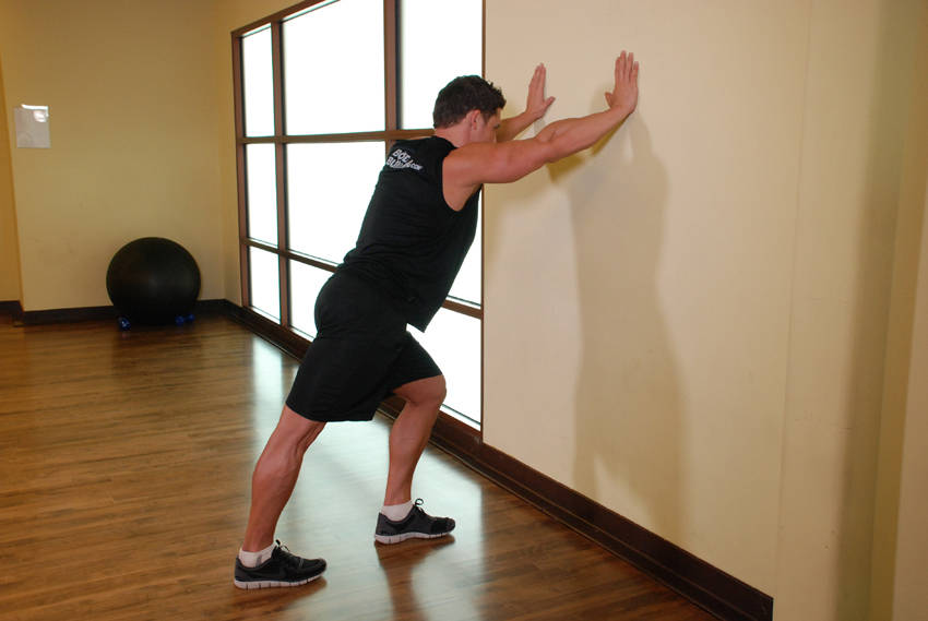 Demonstration of Calf Stretch Hands Against Wall exercise showing proper form and technique