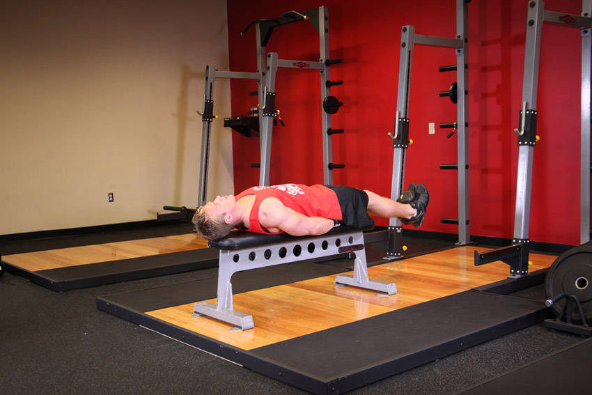 Demonstration of Flat Bench Lying Leg Raise exercise showing proper form and technique