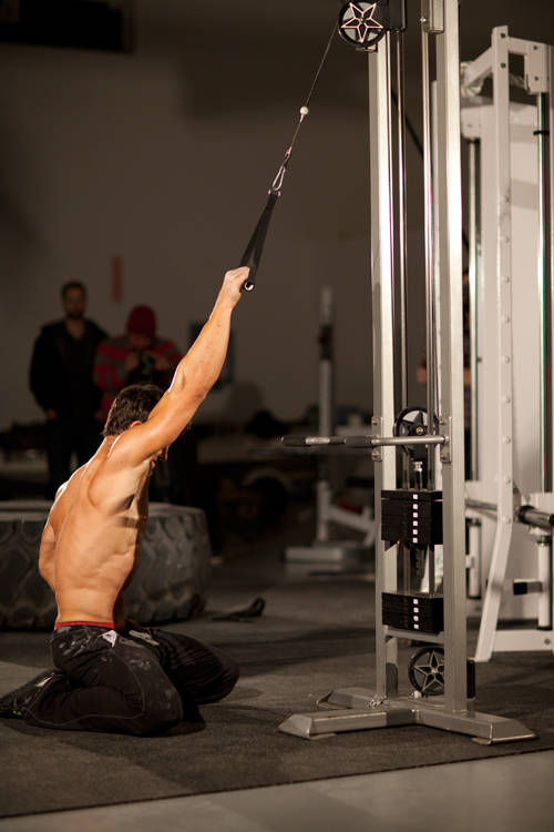 Demonstration of Kneeling Single-Arm High Pulley Row exercise showing proper form and technique