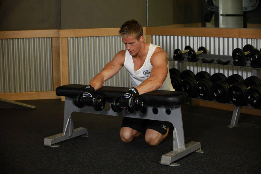 Demonstration of Palms-Down Dumbbell Wrist Curl Over A Bench exercise showing proper form and technique