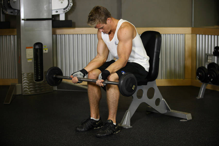 Demonstration of Seated Palm-Up Barbell Wrist Curl exercise showing proper form and technique