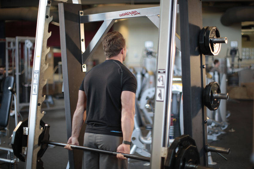 Demonstration of Smith Machine Behind the Back Shrug exercise showing proper form and technique