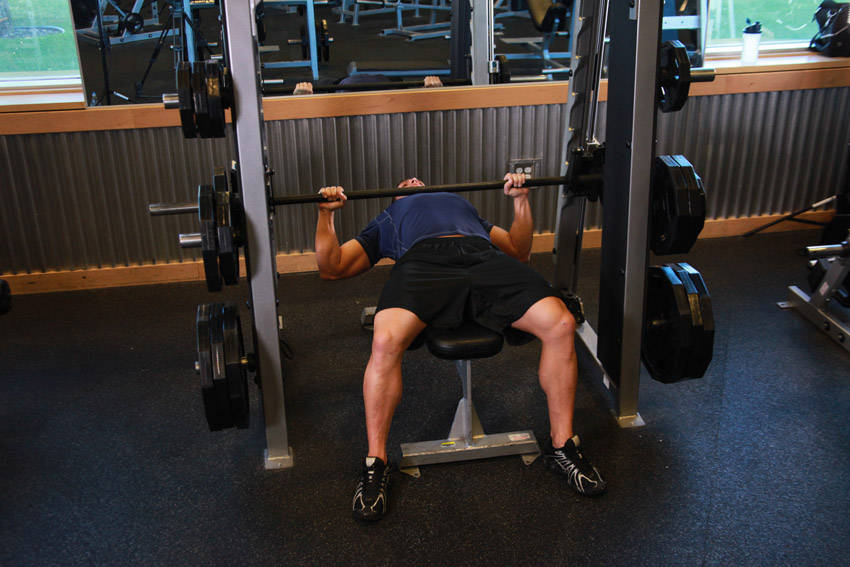 Demonstration of Smith Machine Bench Press exercise showing proper form and technique