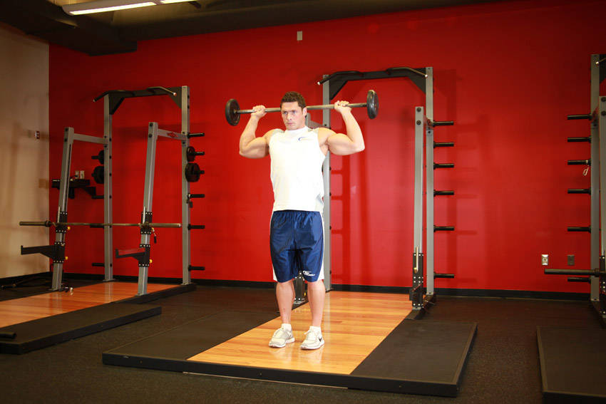 Demonstration of Standing Barbell Press Behind Neck exercise showing proper form and technique