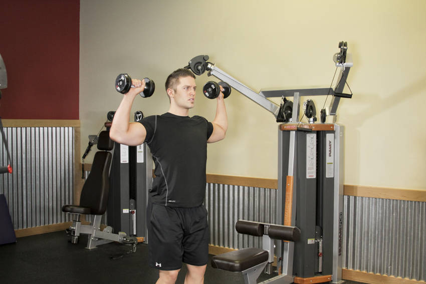 Demonstration of Standing Dumbbell Press exercise showing proper form and technique