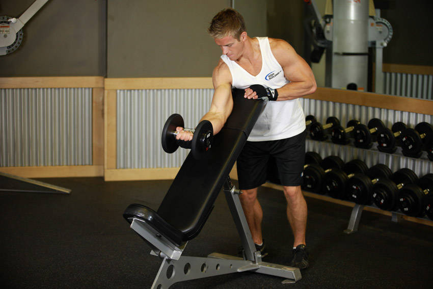 Demonstration of Standing One-Arm Dumbbell Curl Over Incline Bench exercise showing proper form and technique