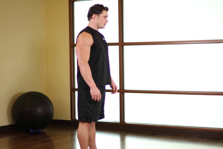 Demonstration of Standing Pelvic Tilt exercise showing proper form and technique