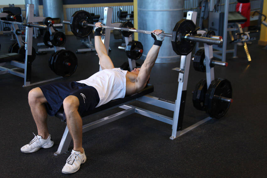Demonstration of Wide-Grip Barbell Bench Press exercise showing proper form and technique